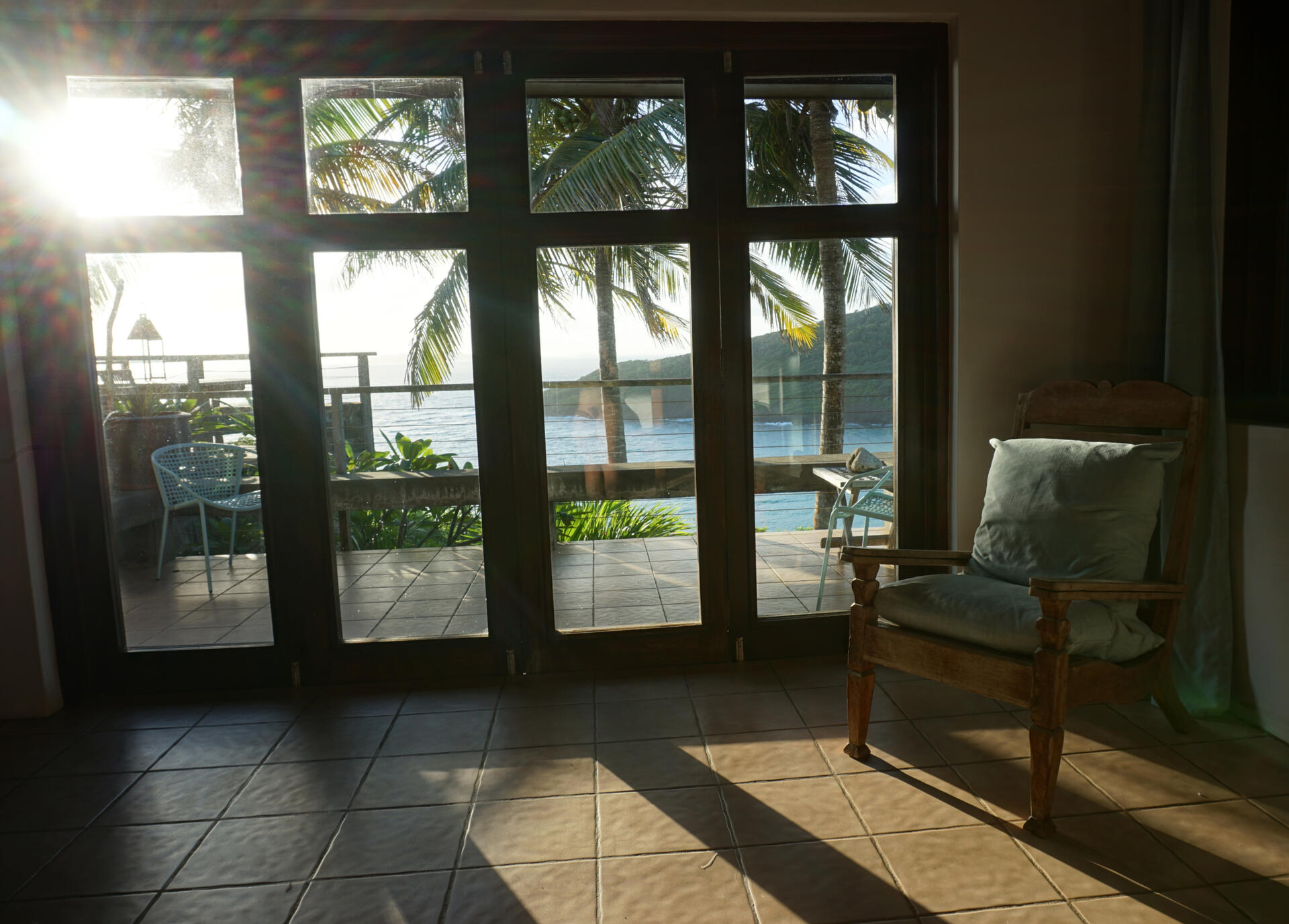 Primary Bedroom view through glass doors to the balcony with palm trees and water in the background.